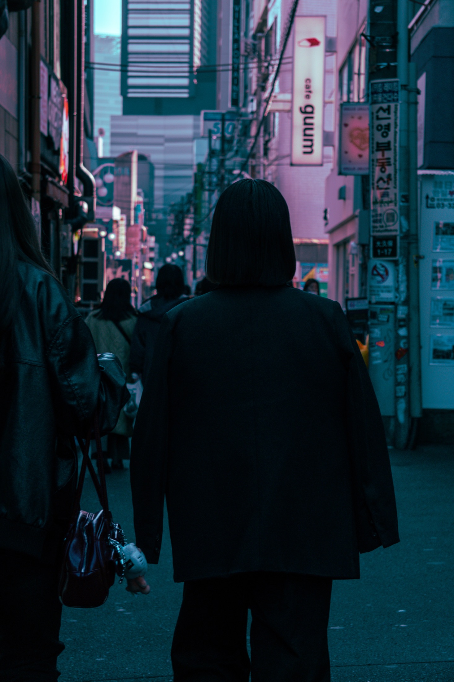 Hooded figure walking away down a neon-lit alley